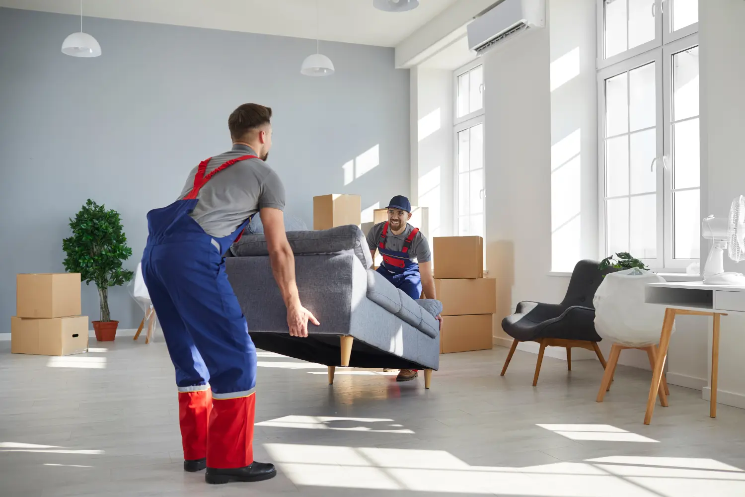 Fröhliche junge Mitarbeiter der Umzugsfirma heben ein schweres Sofa hoch.